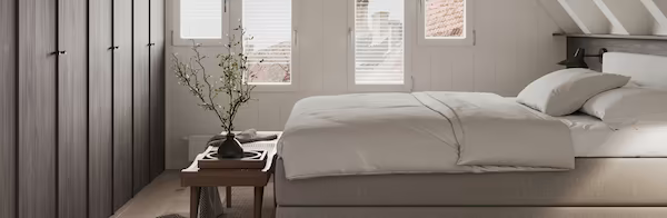 Cozy modern bedroom featuring a neutral bed, wooden bench with a vase, and built-in dark wardrobes.