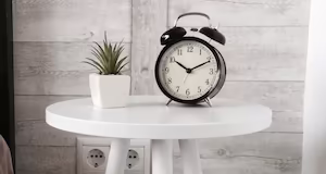 A modern white bedside table with a black alarm clock on top