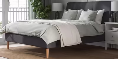 A simple dark grey upholstered bed frame with grey and white sheets