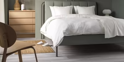 A simple grey-with-a-hint-of-green upholstered bed frame with stark white sheets and pillows