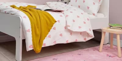 A simple kids bed frame painted white with pink polka-dot patterns on the sheets